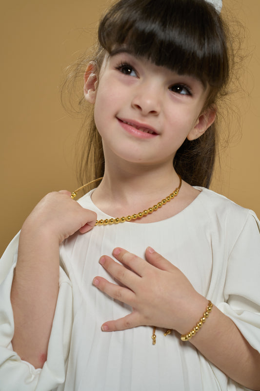 Eternal Heartbeat necklace on a young girl: close-up of gold beaded necklace and matching bracelet.