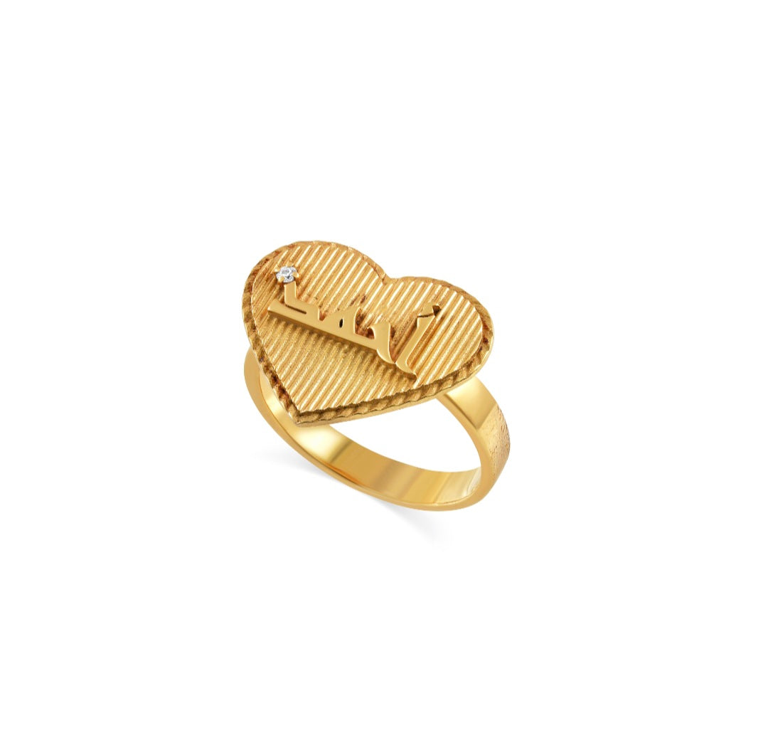 His initial Sirr ring — gold heart-shaped textured top with raised script and small round stone