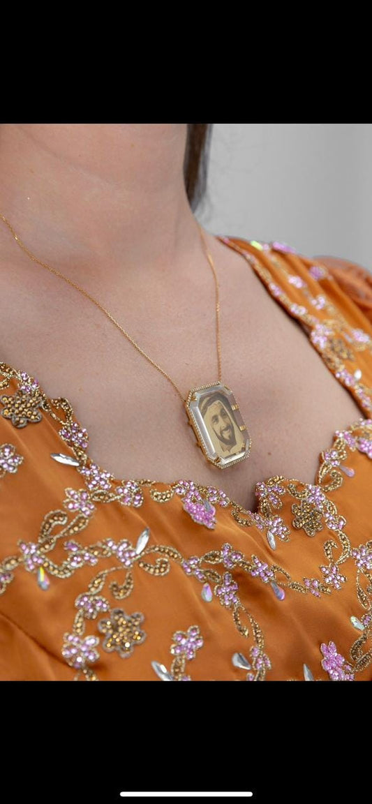 Close-up neckline view of a gold-tone rectangular picture pendant with visible portrait insert on a fine chain.