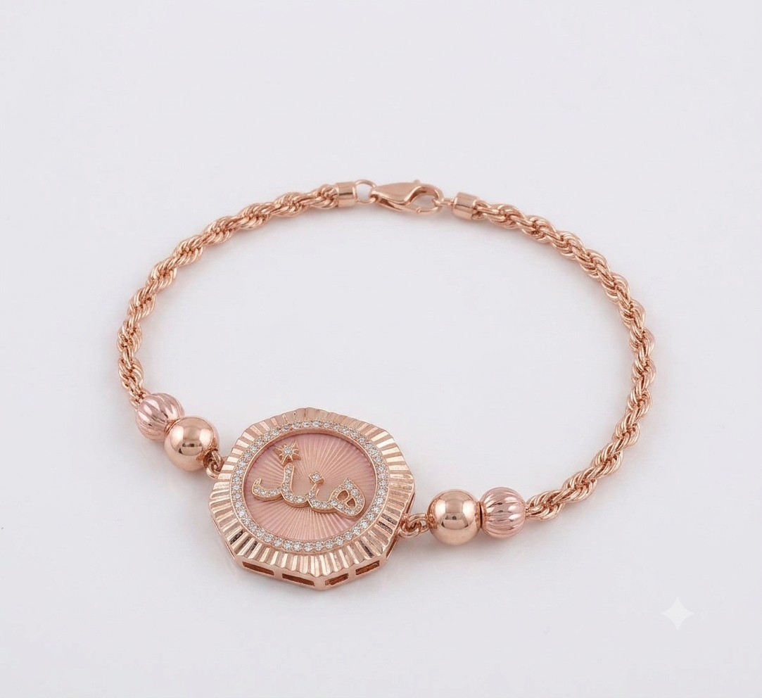 Rose-gold braided bracelet with fluted octagonal medallion, scripted center and crystal halo.