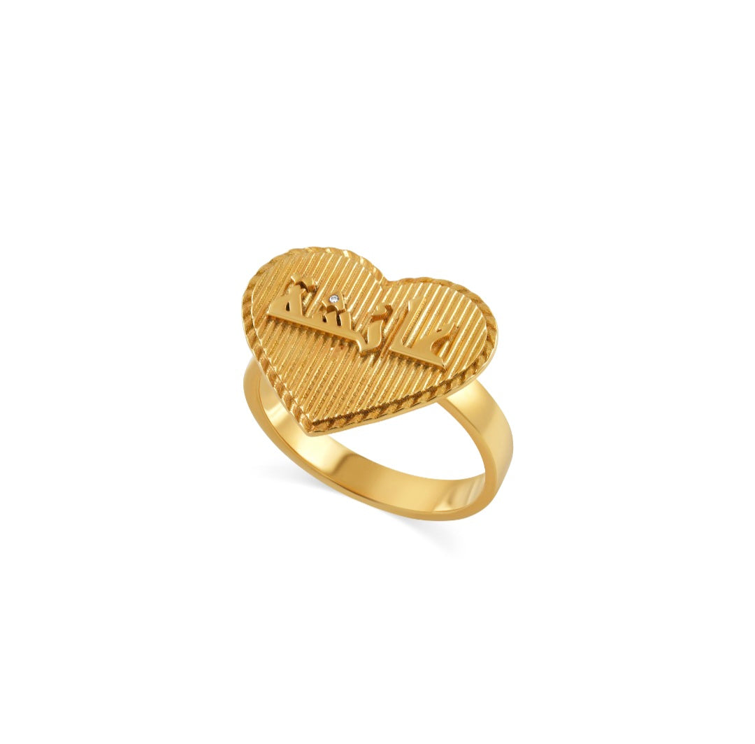 Gold heart-shaped ring with ribbed top, raised script-like initials and a tiny clear stone.