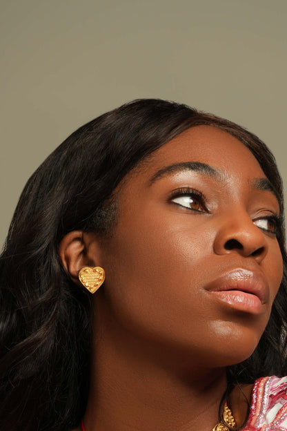 Close-up of a woman's face showing a textured gold heart stud earring on her left ear